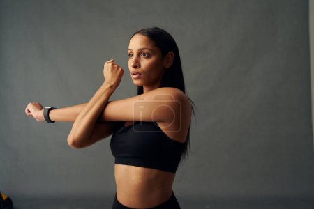 Photo for Focused young biracial woman wearing sports bra doing cross arm stretch in studio - Royalty Free Image