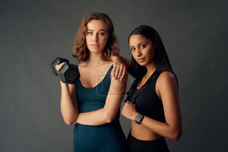Foto de Determined young woman with friend wearing sports clothing looking at camera while holding dumbbell - Imagen libre de derechos