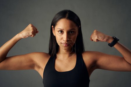 Foto de Portrait of young biracial woman wearing sports bra and fitness tracker flexing bicep muscles in studio - Imagen libre de derechos
