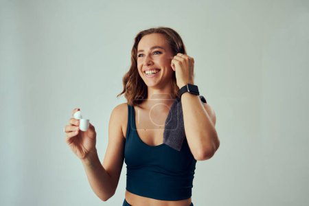 Téléchargez les photos : Young caucasian woman wearing sports clothing smiling while holding wireless headphones and towel - en image libre de droit