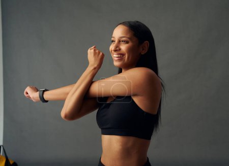 Téléchargez les photos : Happy young biracial woman wearing sports bra doing cross arm stretch in studio - en image libre de droit