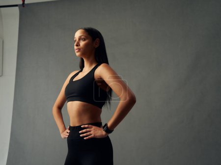 Téléchargez les photos : Focused young biracial woman wearing sports clothing and fitness tracker with hands on hips in studio - en image libre de droit