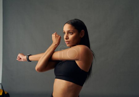 Téléchargez les photos : Determined young biracial woman wearing sports bra doing cross arm stretch in studio - en image libre de droit