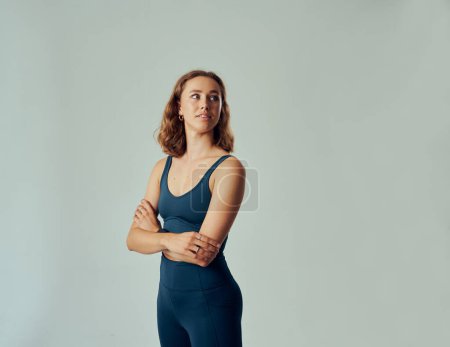 Foto de Young caucasian woman wearing sports clothing looking over shoulder with arms crossed in studio - Imagen libre de derechos