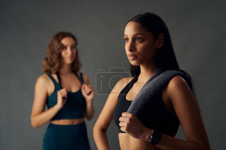 Foto de Young women wearing sports clothing holding towel over shoulder while looking away during break in studio - Imagen libre de derechos
