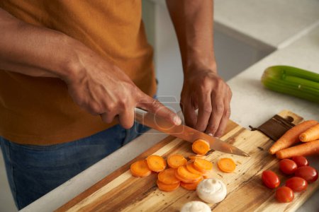Photo for Close-up of young biracial man wearing casual clothing cutting vegetables on chopping board in kitchen - Royalty Free Image