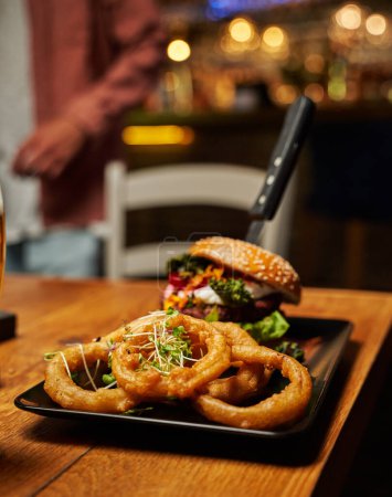 Photo for Close-up of young caucasian man wearing casual clothing with burger and onion rings on table - Royalty Free Image