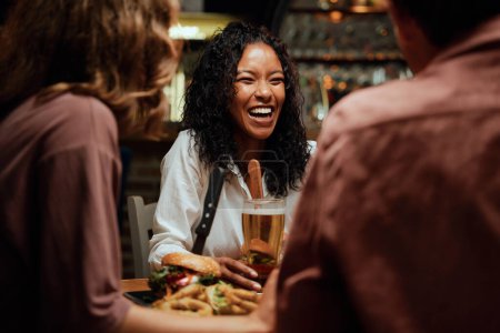 Photo for Happy young multiracial group of friends wearing casual clothing laughing during dinner at restaurant - Royalty Free Image