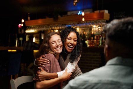 Foto de Feliz joven grupo multirracial de amigos con ropa casual abrazándose en el restaurante - Imagen libre de derechos