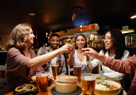 Foto de Joven grupo multirracial de amigos que usan ropa casual disfrutando de comida y bebidas en el restaurante - Imagen libre de derechos