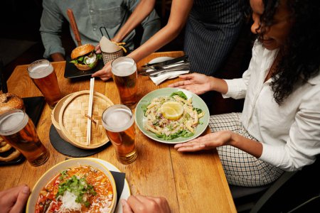 Foto de Primer plano de un joven grupo multirracial de amigos con ropa casual que reciben la cena de la camarera - Imagen libre de derechos