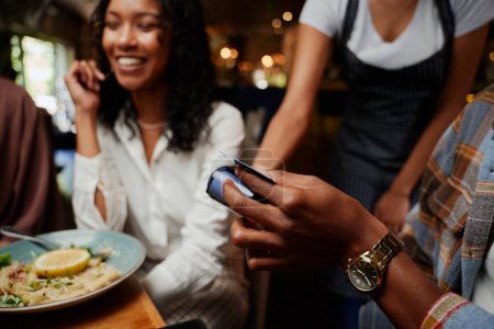 Foto de Primer plano de amigos multirraciales felices usando ropa casual pagando camarera para la cena en el restaurante - Imagen libre de derechos