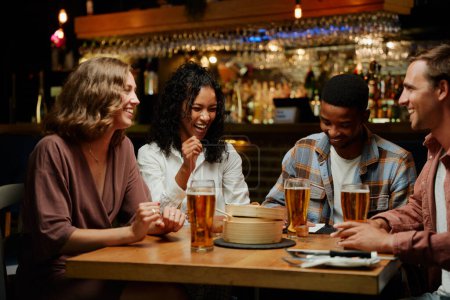 Foto de Feliz joven grupo multirracial de amigos con ropa casual riéndose durante la cena en el restaurante - Imagen libre de derechos
