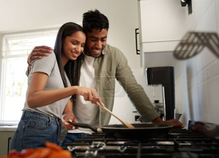 Foto de Feliz joven pareja biracial con ropa casual cocinar alimentos en cacerola sobre la estufa en la cocina - Imagen libre de derechos