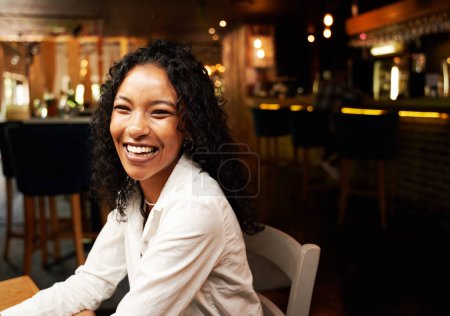 Glückliche junge Frau in lässiger Kleidung lächelt beim Abendessen im Restaurant am Tisch
