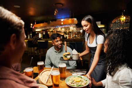 Glückliche junge multiethnische Gruppe von Freunden in lässiger Kleidung lächelt, während sie das Abendessen von der Kellnerin erhält