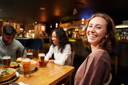 Téléchargez les photos : Jeune groupe multiracial d'amis portant des vêtements décontractés souriant autour de la table au restaurant - en image libre de droit