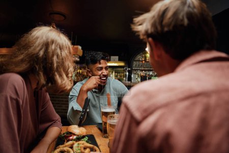 Téléchargez les photos : Jeune groupe multiracial d'amis portant des vêtements décontractés riant pendant la conversation pendant le dîner - en image libre de droit