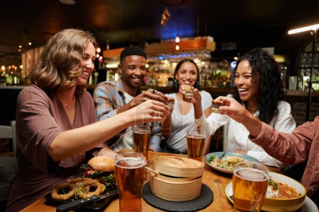 Young multiracial group of friends wearing casual clothing enjoying dinner and drinks at restaurant