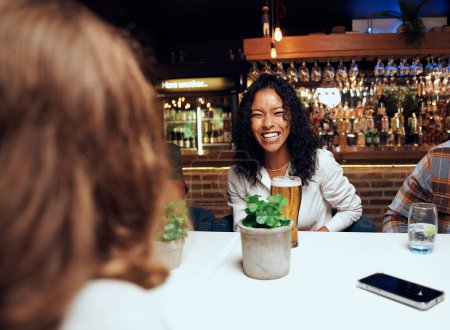 Foto de Feliz joven grupo multirracial de amigos con ropa casual riendo con bebidas por mesa en el bar - Imagen libre de derechos