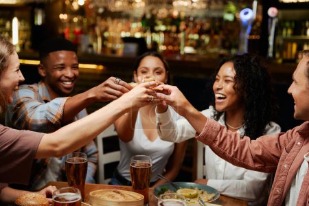 Young multiracial group of friends wearing casual clothing enjoying celebratory toast at restaurant