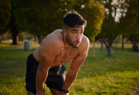 Photo for Shirtless young biracial man looking away and exhaling by trees in the park - Royalty Free Image