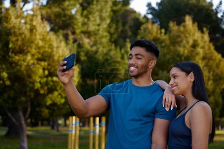 Téléchargez les photos : Heureux jeune couple multiracial portant des vêtements de sport souriant tout en prenant selfie avec téléphone portable dans le parc - en image libre de droit