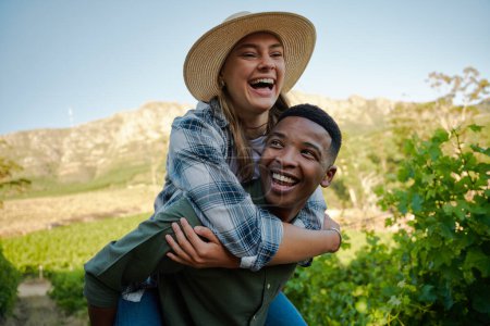 Foto de Feliz joven pareja multirracial con ropa casual sonriendo mientras da a cuestas en la granja - Imagen libre de derechos