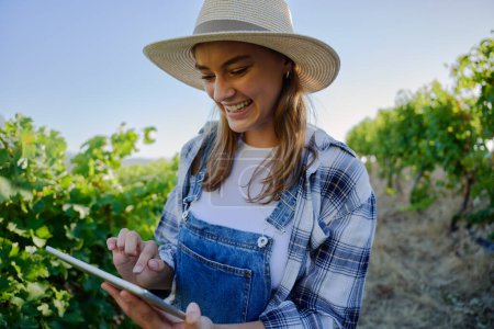 Foto de Feliz joven caucásico mujeres usando ropa casual usando tableta digital al lado de las plantas en la granja - Imagen libre de derechos