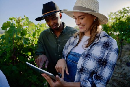 Téléchargez les photos : Jeune couple multiracial portant des vêtements décontractés souriant tout en utilisant une tablette numérique par des plantes à la ferme - en image libre de droit