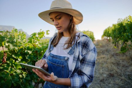 Téléchargez les photos : Jeunes femmes caucasiennes portant des vêtements décontractés en utilisant une tablette numérique à côté de plantes à la ferme - en image libre de droit