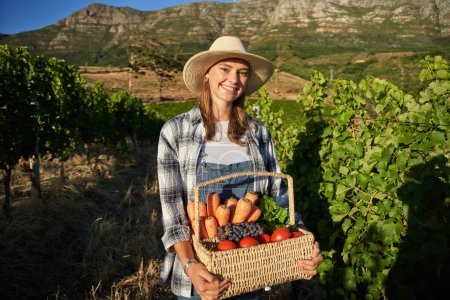 Photo for Young caucasian woman wearing casual clothing carrying basket with fresh fruit and vegetable on farm - Royalty Free Image