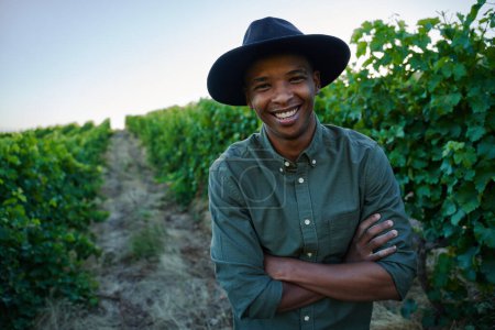 Foto de Feliz joven negro vestido con ropa casual con los brazos cruzados al lado de los cultivos en la granja - Imagen libre de derechos
