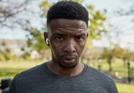 Téléchargez les photos : Portrait de jeune homme noir portant des vêtements de sport avec des écouteurs sans fil transpirant après l'exercice dans le parc - en image libre de droit