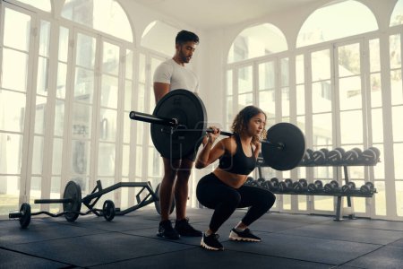 Foto de Dos adultos jóvenes multirraciales en forma usando ropa deportiva haciendo entrenamiento con pesas en el gimnasio - Imagen libre de derechos