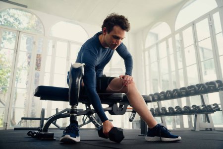 Foto de Joven hombre caucásico con extremidad artificial haciendo ejercicios de entrenamiento con pesas en el gimnasio - Imagen libre de derechos