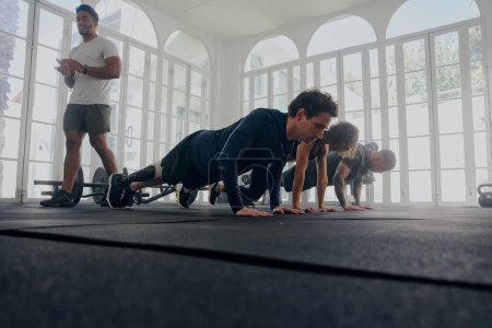 Photo for Trainer applauding group of multiracial young adults wearing sports clothing doing push-ups at the gym - Royalty Free Image