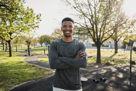 Photo for Happy young black man wearing sports clothing looking at camera with arms crossed in park - Royalty Free Image