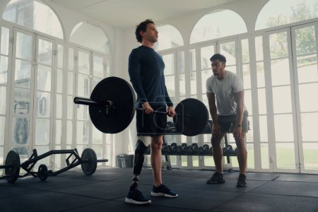 Foto de Entrenador multiracial haciendo ejercicios de entrenamiento con pesas con un joven con una pierna protésica en el gimnasio - Imagen libre de derechos