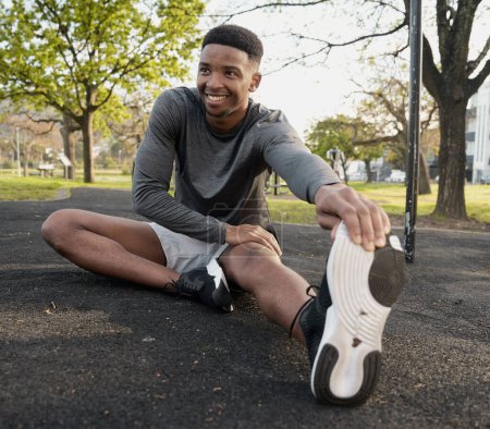 Photo for Happy young black man wearing sports clothing sitting and doing stretches in park - Royalty Free Image