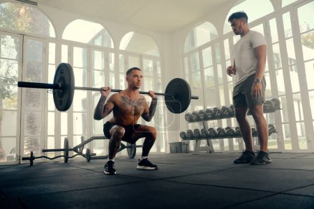 Foto de Dos jóvenes atléticos multirraciales que usan ropa deportiva haciendo entrenamiento con pesas en el gimnasio - Imagen libre de derechos