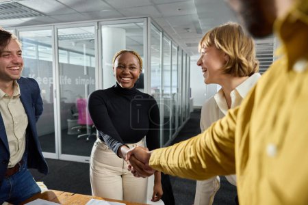 Photo for Four happy young multiracial adults wearing businesswear shaking hands in conference room in office - Royalty Free Image