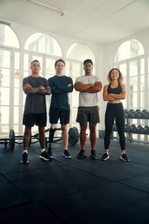 Foto de Grupo de jóvenes adultos multirraciales con ropa deportiva mirando a la cámara con los brazos cruzados en el gimnasio - Imagen libre de derechos