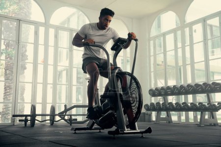Foto de Atlético joven multirracial hombre usando ropa deportiva ciclismo en bicicleta estática en el gimnasio - Imagen libre de derechos