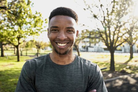 Téléchargez les photos : Portrait de jeune homme noir heureux portant des vêtements de sport regardant la caméra et souriant dans le parc - en image libre de droit