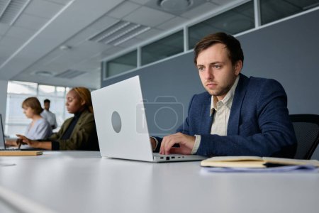 Téléchargez les photos : Quatre jeunes hommes d'affaires multiraciaux portant des vêtements d'affaires travaillant au bureau derrière des ordinateurs portables au bureau - en image libre de droit