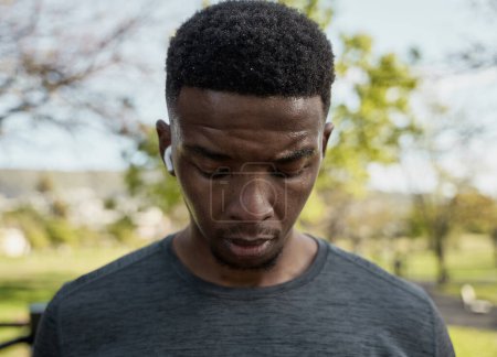 Foto de Retrato de un joven negro usando ropa deportiva con auriculares inalámbricos sudando en el parque - Imagen libre de derechos