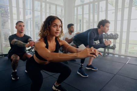 Group of focused multiracial young adults wearing sports clothing doing squats at the gym