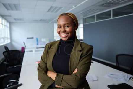 Foto de Joven empresaria negra confiada que usa ropa de negocios con los brazos cruzados al lado del escritorio en la oficina corporativa - Imagen libre de derechos
