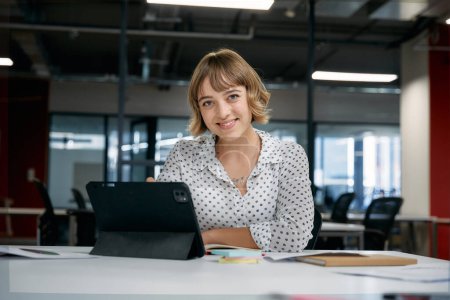 Foto de Feliz joven mujer de negocios caucásica sonriendo mientras usa la tableta digital durante la reunión en la oficina corporativa - Imagen libre de derechos